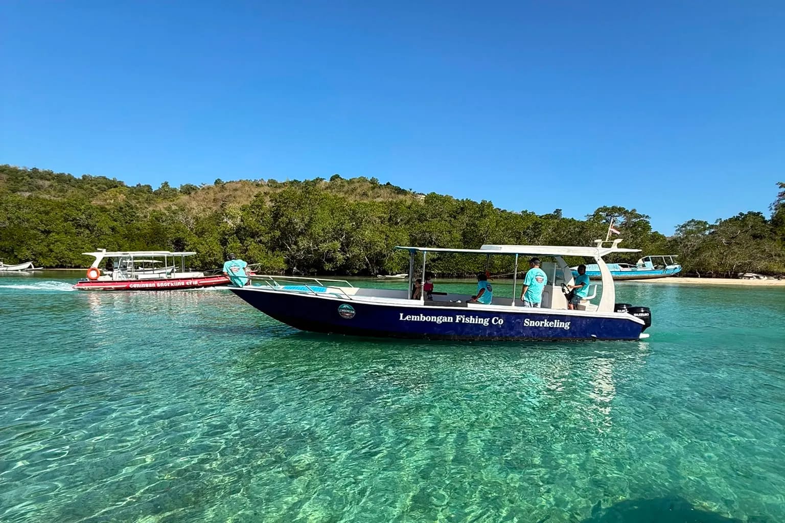 The Lembongan Fishing Co fiberglass boat with its canopy and crew on clear turquoise water