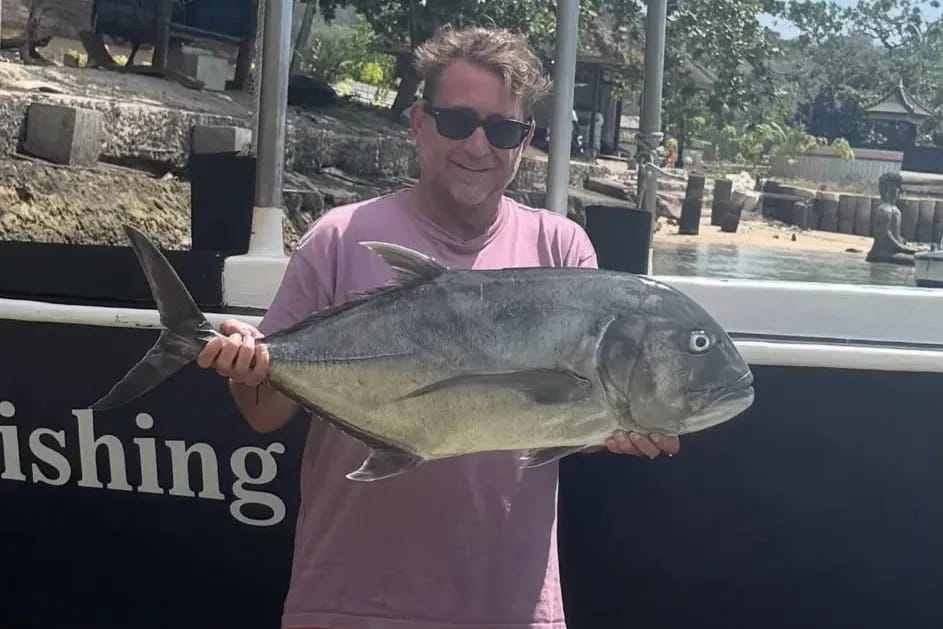 A guest on board holding a giant trevally caught on a charter